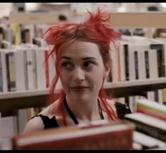 a woman with red hair is in front of bookshelves and looking at the camera