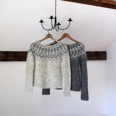 two sweaters hanging on a wooden hanger next to a chandelier in a white room