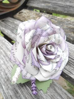 a purple and white rose sitting on top of a wooden bench next to an old book page