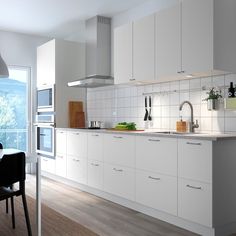 a kitchen with white cabinets and wooden flooring next to a dining table in front of an open window