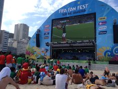 people sitting in the sand watching a tennis match on a large screen at a beach