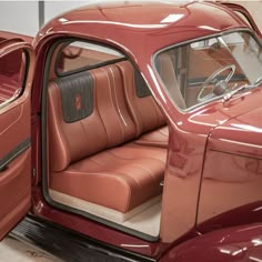 the interior of an old red car with its door open and seat folded down in front