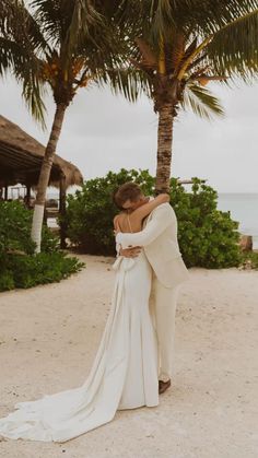 a bride and groom embracing on the beach in front of palm trees at their destination