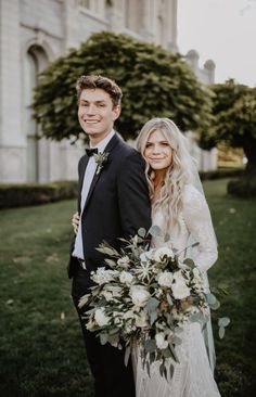 a bride and groom standing in front of a building with greenery on the lawn