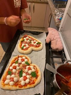 two uncooked pizzas with mozzarella and basil on them sitting on top of a stove