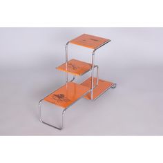 three tiered metal and wood table with orange paint on the top, in front of a white background