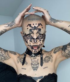 a woman with tattoos on her face and chest holding her hands up to her head