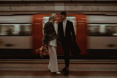 a man and woman standing next to each other in front of a train