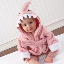 a baby wearing a pink shark robe on top of a white rug in front of a wall