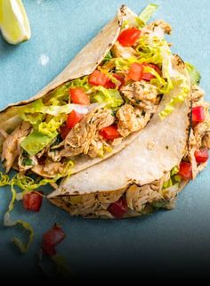 three tortillas with chicken, lettuce and tomatoes on a blue surface