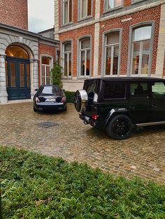 two black cars parked in front of a brick building on a cobblestone street