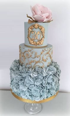 a three tiered blue and gold wedding cake with flowers on the top, sitting on a table