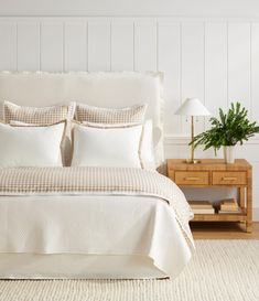 a bed with white sheets and pillows next to a night stand on a rug in a bedroom