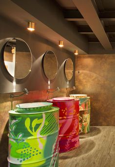 three brightly colored buckets are lined up on the floor in front of two mirrors