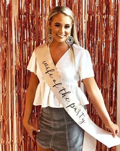 a woman in a white shirt and grey skirt posing for the camera with a sash around her waist