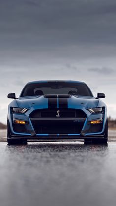 the front end of a blue sports car on a wet road with dark clouds in the background