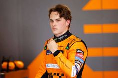 a young man in an orange racing suit is adjusting his collar and looking off to the side