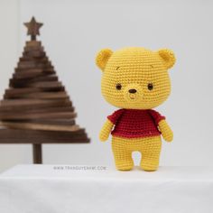 a crocheted teddy bear standing next to a small christmas tree on a table