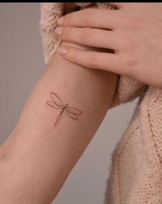 a woman's arm with a small dragonfly tattoo on the left side of her arm