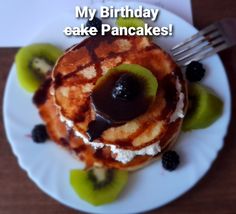 a white plate topped with pancakes covered in chocolate sauce and kiwis next to a fork