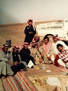 a group of men sitting on top of a blanket in front of a white truck