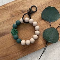 a wooden cutting board topped with a green and white beaded bracelet next to a pair of scissors