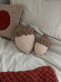 two knitted pillows sitting on top of a bed next to an orange and white pillow