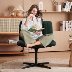 a woman sitting in a green chair reading a book while holding her hand up to her face