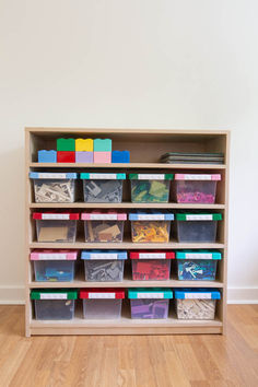 a wooden shelf filled with lots of different colored bins and plastic containers on top of it