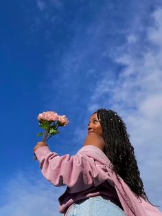 a woman is holding a flower in her right hand and looking up into the sky