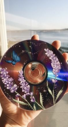 a person holding up a cd with purple flowers on the front and blue butterflies on the back