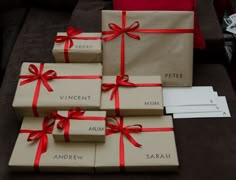 four wrapped presents sitting on top of a couch with red ribbon around them and the names of each present