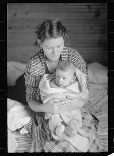 an old photo of a woman holding a baby in her arms and looking at the camera