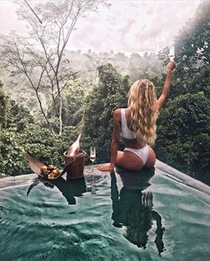 a woman sitting on the edge of a pool holding a glass of wine in her hand