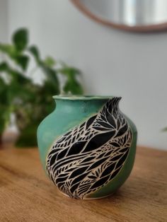 a green vase sitting on top of a wooden table next to a potted plant