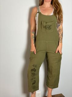 Super cute and comfy, these oversized olive green overalls will become an instant favorite. Tie closure, front and side patch pockets. Printed on both front and back legs  and chest pocket with our hand-drawn mushroom designs. Available in S/M, L/XL and XXL. Model is a women's medium/large and wearing a S/M.  50% Viscose, 30% Hemp, 20% Cotton, ethically made. Machine wash cold. Tumble dry low or line dry. Green Casual Cotton Overalls, Casual Green Cotton Overalls, Casual Green Jumpsuits And Rompers With Side Pockets, Green Relaxed Fit Overalls, Casual Green Overalls With Pockets, Green Bib Front Overalls With Pockets, Green Bib Front Jumpsuit With Pockets, Green Jumpsuit With Pockets And Bib Front, Green Relaxed Fit Overalls With Pockets