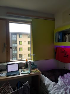 a laptop computer sitting on top of a desk in front of a window next to a bed