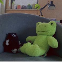 two stuffed animals sitting on a chair in the living room, one black and one green