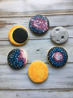 six decorated cookies arranged in the shape of planets on a wooden table with white and blue paint