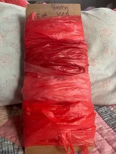 a piece of red string wrapped in plastic sitting on top of a bed