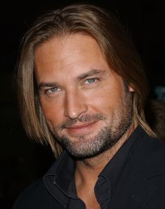 a close up of a person with long hair and a beard wearing a black shirt