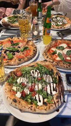 three pizzas on plates with different toppings sitting on a table next to drinks