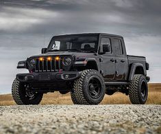 a black jeep parked on the side of a road with dark clouds in the background