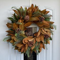 a wreath with pine cones and green leaves on a front door sill by a white door