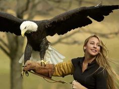 a woman holding an eagle on her arm with it's wings spread wide open