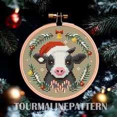 a cross stitch christmas ornament with a cow wearing a santa hat on it