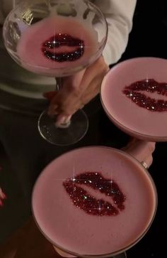 two wine glasses filled with pink liquid and the word lips painted on them are being held by someone's hands