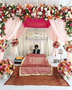 a man sitting on top of a bed under a canopy covered in pink and orange flowers