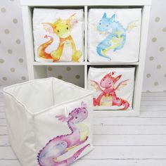 three different colored dragon designs on white canvass in a storage bin with polka dot wallpaper