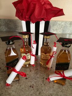 four bottles of liquor tied with red ribbon and two white candles are sitting in front of a gift box